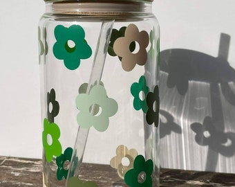 May include: A clear glass reusable water bottle with a bamboo lid and a green and brown floral pattern. The bottle comes with a clear plastic straw.