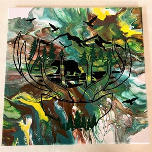 May include: Abstract painting on canvas with a green, brown, and yellow color scheme. The painting features a silhouette of a deer's antlers with a bear inside the antlers. The antlers are surrounded by a forest scene with trees and mountains.