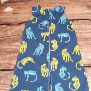 May include: A blue sleeveless sleep sack with a repeating pattern of yellow and teal leopards. The sleep sack has a zipper down the back.