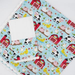 May include: A light blue fabric with a white gingham pattern featuring a farm theme print of red barns, black and white cows, pink pigs, white sheep, and yellow ducks. The fabric has a white crochet lace trim along the scalloped edges.