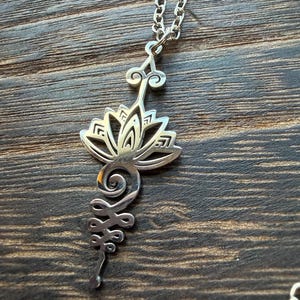 May include: A set of three ceramic mugs with a speckled, cream-colored glaze. Each mug features a different hand-painted design: a blue and green leaf, a yellow sun, and a pink flower. The mugs have a simple, modern design.