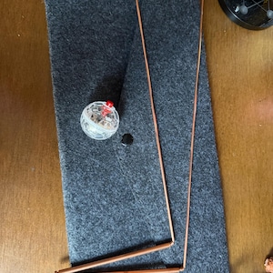 May include: A collection of items including two copper rods, a clear, round, faceted object with a red top, a small black disc, and a gray felt mat. The rods are bent at right angles. The items are arranged on a wooden surface.