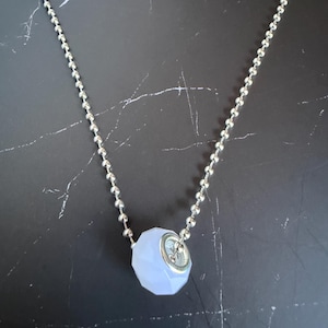 May include: A silver-toned ball chain necklace featuring a single faceted, light blue, translucent bead pendant. The bead is secured with a metallic silver-colored cap and ring, creating a simple and clean design for this piece of jewelry.