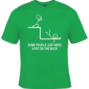 May include: Green t-shirt featuring a white stick figure design. The design depicts one stick figure pushing another stick figure off a ledge. The text reads "Some people just need a pat on the back."