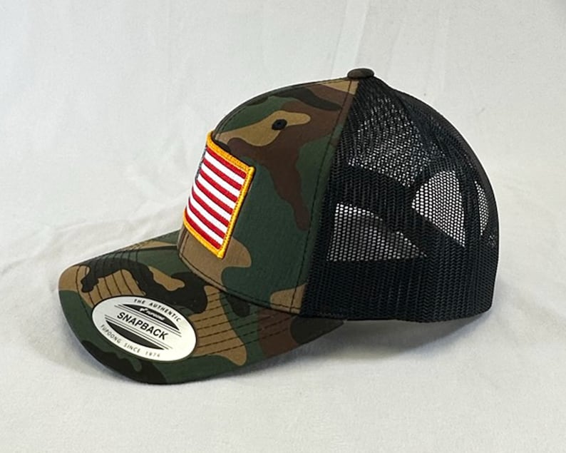 May include: A camouflage trucker hat with a black mesh back and a small American flag patch on the front. The hat has a sticker on the side that says "The Authentic Snapback, Fitted Since 1974."