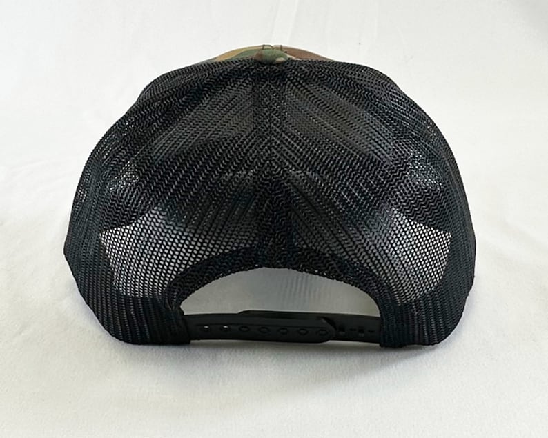May include: A black and green camouflage trucker hat with a black mesh back. The hat has a black adjustable strap.