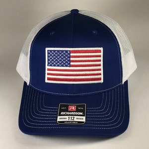 May include: A blue and white trucker hat with a red, white, and blue American flag patch on the front. The hat has a mesh back and says "Richardson" and "Original 112 Trucker" on the back.