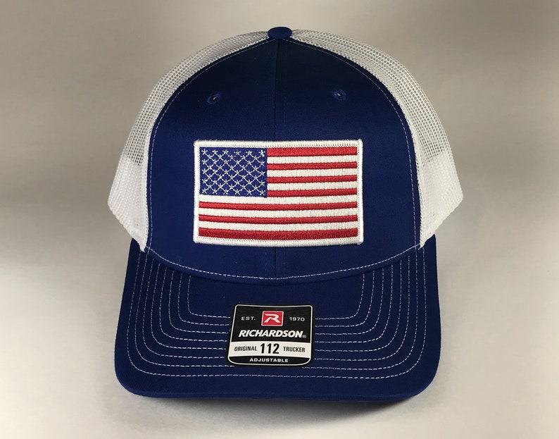 May include: A blue and white trucker hat with a red, white, and blue American flag patch on the front. The hat has a mesh back and says "Richardson" and "Original 112 Trucker" on the back.