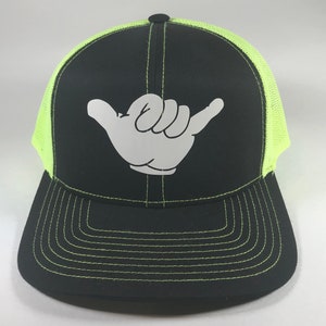 May include: Black trucker hat with a neon green mesh back and a white hand making the shaka sign.