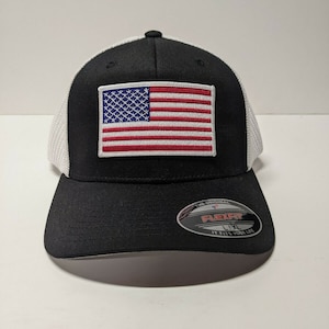 May include: Black and white mesh baseball cap with an American flag patch on the front. The cap has a Flexfit label on the side with the text "The Original Flexfit 1XL It Fits Your Life".