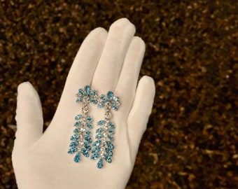 May include: A pair of long, teardrop-shaped dangle earrings with blue and clear crystal stones.