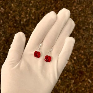 May include: A pair of silver dangle earrings with red square-shaped gemstones.