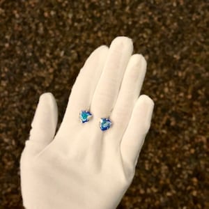 May include: A pair of blue crystal earrings with a silver setting. The earrings are displayed on a white glove.