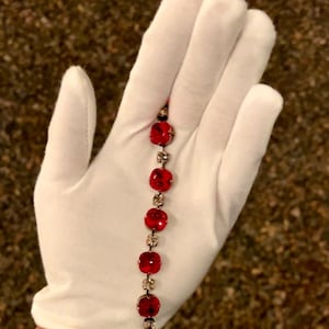 May include: A red crystal bracelet with silver accents. The bracelet is made of small, round crystals that are connected by a silver chain.