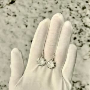 May include: A pair of silver earrings with a white stone surrounded by smaller stones.