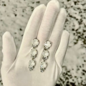 May include: A pair of silver dangle earrings with three white round stones on each earring.