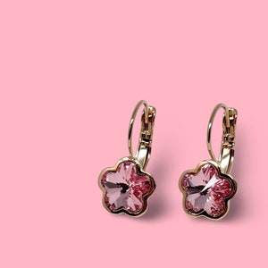 May include: A pair of gold hoop earrings with pink flower-shaped crystal accents.