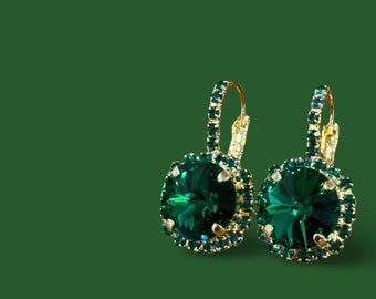 May include: A pair of gold earrings with emerald green crystal stones. The earrings have a dangling design with a round stone in the center.