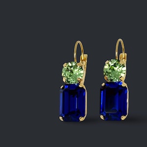 May include: A pair of gold-toned earrings featuring a green, round-cut stone above a large, rectangular, deep blue stone. The earrings have a lever-back closure and are set against a dark background.