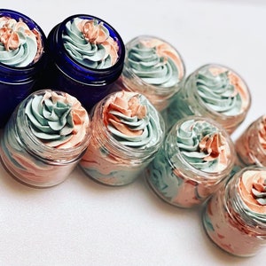 May include: A collection of small glass jars filled with a swirl of light pink and light green whipped cream. The jars are arranged in a row on a white surface.
