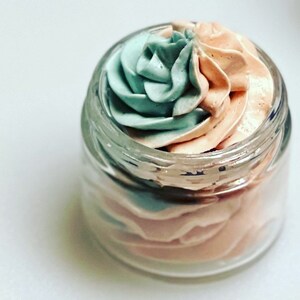 May include: A glass jar filled with a swirl of light blue and peach-coloured whipped body butter.