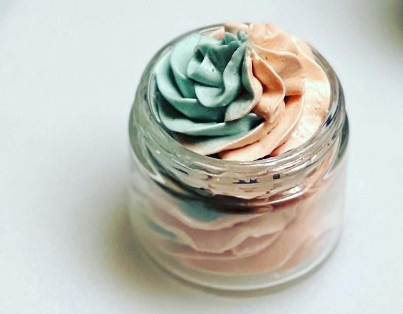 May include: A glass jar filled with a swirl of light blue and peach-coloured whipped body butter.
