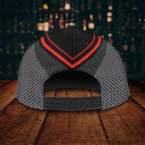 May include: Black and gray baseball cap with a red chevron design on the crown. The cap features a mesh pattern on the sides and a black adjustable snapback closure. The cap is displayed on a wooden surface.
