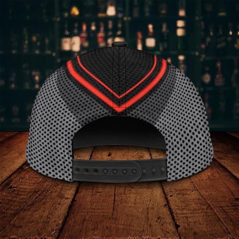 May include: Black and gray baseball cap with a red chevron design on the crown. The cap features a mesh pattern on the sides and a black adjustable snapback closure. The cap is displayed on a wooden surface.