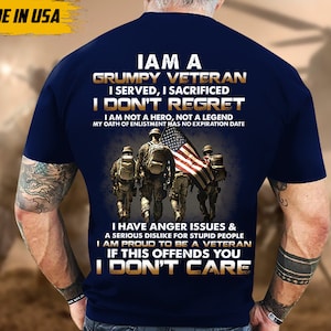 May include: Navy blue t-shirt with a graphic featuring a group of soldiers carrying the American flag. Text on the shirt reads "I am a Grumpy Veteran" and other statements. "Made in USA" is printed on the top left.