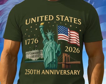May include: Olive green t-shirt featuring a graphic celebrating the 250th anniversary of the United States. The design includes the Statue of Liberty, the American flag, the White House, and the Brooklyn Bridge, with the years 1776 and 2026.
