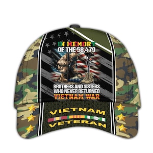 May include: Camouflage baseball cap with a design commemorating the Vietnam War. The cap features an American flag, a soldier kneeling, and the text "In Memory of the 58,479." It also includes the words "Vietnam Veteran."