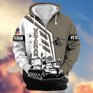 Pode incluir: Um casaco com capuz e z&iacute;per com tema militar. O design apresenta um tanque, helic&oacute;pteros e a palavra "VETERAN" em letras grandes. A bandeira americana est&aacute; na manga esquerda e a palavra "VETE" na manga direita.