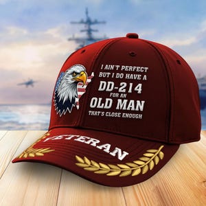 May include: Maroon baseball cap featuring an American bald eagle graphic with an American flag design. The cap has the text "I ain't perfect but I do have a DD-214 for an old man that's close enough" and "Veteran".