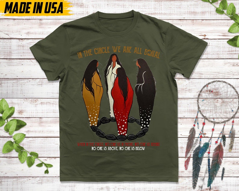 Puede incluir: Camiseta verde oliva con el texto "IN THE CIRCLE WE ARE ALL EQUAL" y "NO ONE IS ABOVE, NO ONE IS BELOW." La camiseta presenta una ilustraci&oacute;n de tres figuras en marr&oacute;n, blanco y rojo, de pie en un c&iacute;rculo. "MADE IN USA" est&aacute; impreso en la parte superior.