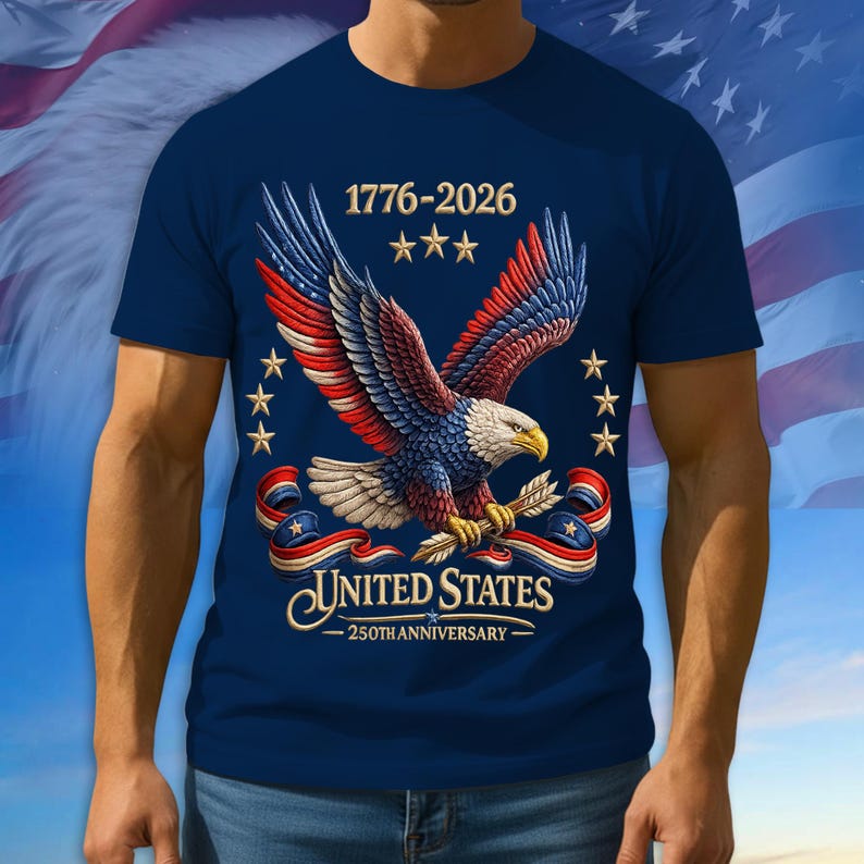 Puede incluir: Camiseta azul marino con una ilustraci&oacute;n detallada de un &aacute;guila con alas rojas, blancas y azules, sosteniendo flechas. El texto "1776-2026" y "United States 250th Anniversary" est&aacute;n presentes. Estrellas y cintas patri&oacute;ticas completan el dise&ntilde;o.