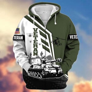 Pode incluir: Um casaco com capuz e z&iacute;per com tema militar. O design apresenta um tanque, helic&oacute;pteros e a palavra "VETERAN" em letras grandes. As cores s&atilde;o branco, verde e preto, com um patch da bandeira americana na manga.