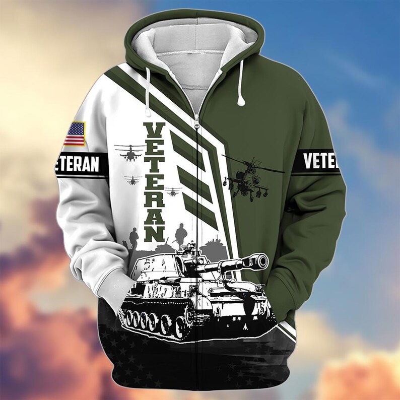 Pode incluir: Um casaco com capuz e z&iacute;per com tema militar. O design apresenta um tanque, helic&oacute;pteros e a palavra "VETERAN" em letras grandes. As cores s&atilde;o branco, verde e preto, com um patch da bandeira americana na manga.