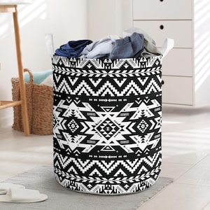 May include: A black and white patterned laundry hamper filled with clothes. The hamper has a geometric design with white handles. The laundry basket is cylindrical and sits on a gray rug.