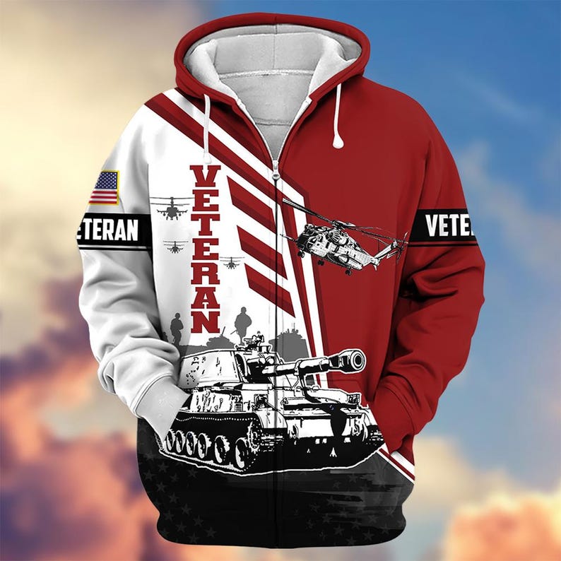Pode incluir: Casaco com capuz e fecho de correr completo com um design patri&oacute;tico. O casaco apresenta um esquema de cores vermelho e branco com um gr&aacute;fico a preto e branco de um tanque e helic&oacute;pteros. A palavra "VETERAN" &eacute; impressa verticalmente na frente.