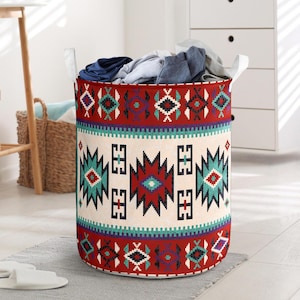 May include: A cylindrical laundry hamper with a Southwestern-inspired design. The hamper features a cream-colored central band with geometric patterns in red, teal, purple, and black. White handles are attached to the top rim, and the hamper is filled with folded clothes.
