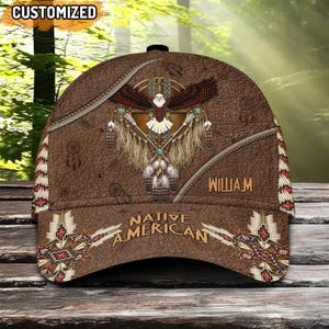 May include: Brown baseball cap with a Native American design. The cap features an eagle with outstretched wings, feathers, and the text "Native American." The word "William" is printed on the side. The top of the cap has the word "Customized".