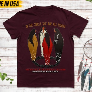 Puede incluir: Camiseta burdeos con el texto "IN THE CIRCLE WE ARE ALL EQUAL". El gr&aacute;fico presenta tres figuras con vestidos dorados, blancos y rojos. El texto "WHEN IN THE CIRCLE, NO ONE IS IN FRONT, NO ONE IS BEHIND. NO ONE IS ABOVE, NO ONE IS BELOW" tambi&eacute;n est&aacute; impreso. "MADE IN USA" est&aacute; impreso en la parte superior.