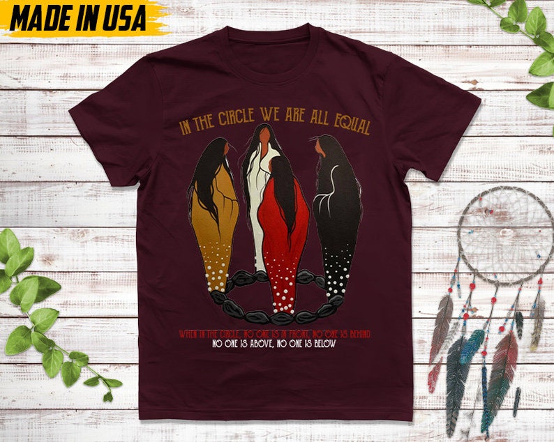 Puede incluir: Camiseta burdeos con el texto "IN THE CIRCLE WE ARE ALL EQUAL". El gr&aacute;fico presenta tres figuras con vestidos dorados, blancos y rojos. El texto "WHEN IN THE CIRCLE, NO ONE IS IN FRONT, NO ONE IS BEHIND. NO ONE IS ABOVE, NO ONE IS BELOW" tambi&eacute;n est&aacute; impreso. "MADE IN USA" est&aacute; impreso en la parte superior.