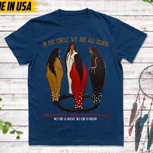 Puede incluir: Una camiseta azul marino con el texto "IN THE CIRCLE WE ARE ALL EQUAL". La camiseta presenta una ilustraci&oacute;n de tres figuras en un c&iacute;rculo. El texto "NO ONE IS ABOVE, NO ONE IS BELOW" tambi&eacute;n est&aacute; impreso.