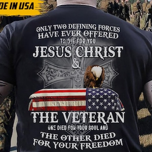 May include: Black t-shirt with the text "ONLY TWO DEFINING FORCES HAVE EVER OFFERED TO DIE FOR YOU JESUS CHRIST & THE VETERAN". The design includes an eagle, a cross, and an American flag. The words "MADE IN USA" are in the upper left corner.