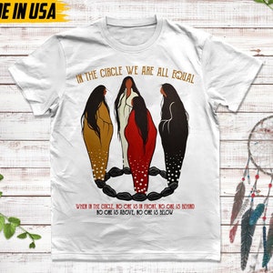 Puede incluir: Camiseta blanca con el texto "IN THE CIRCLE WE ARE ALL EQUAL" y una ilustraci&oacute;n de cuatro figuras en un c&iacute;rculo. El texto "WHEN IN THE CIRCLE, NO ONE IS IN FRONT, NO ONE IS BEHIND, NO ONE IS ABOVE, NO ONE IS BELOW" tambi&eacute;n est&aacute; impreso en la camiseta. "MADE IN USA" est&aacute; impreso en la parte superior izquierda.
