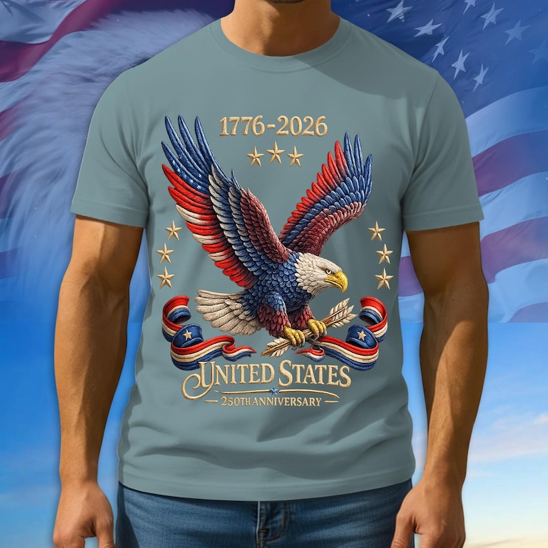 Puede incluir: Camiseta azul claro con un &aacute;guila de alas rojas, blancas y azules, sosteniendo flechas. El texto "1776-2026" y "UNITED STATES - 250TH ANNIVERSARY" tambi&eacute;n est&aacute;n presentes.
