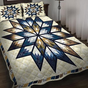 May include: A quilted bedspread and two pillow shams featuring a large starburst design. The starburst is composed of geometric shapes in shades of blue, brown, and cream. The bedding has a diamond pattern and a decorative border.