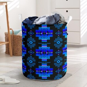 May include: A round laundry hamper with a black background and a repeating blue geometric pattern. The hamper is filled with folded clothes and has white handles. The hamper is sitting on a gray rug.