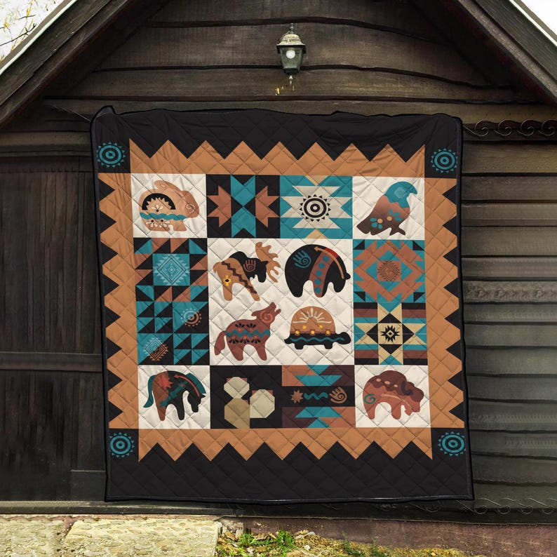 May include: A black and tan quilt with a Native American design. The quilt features various animal and geometric patterns in shades of teal, brown, and cream. The quilt is hanging on a wooden wall.